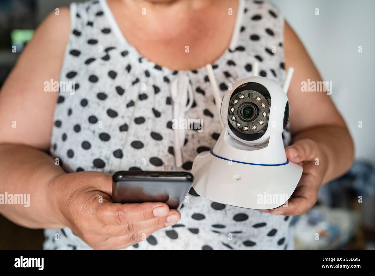 Close up on midsection of unknown woman holding home security surveillance camera and mobile phone trying to install an app front view copy space Stock Photo