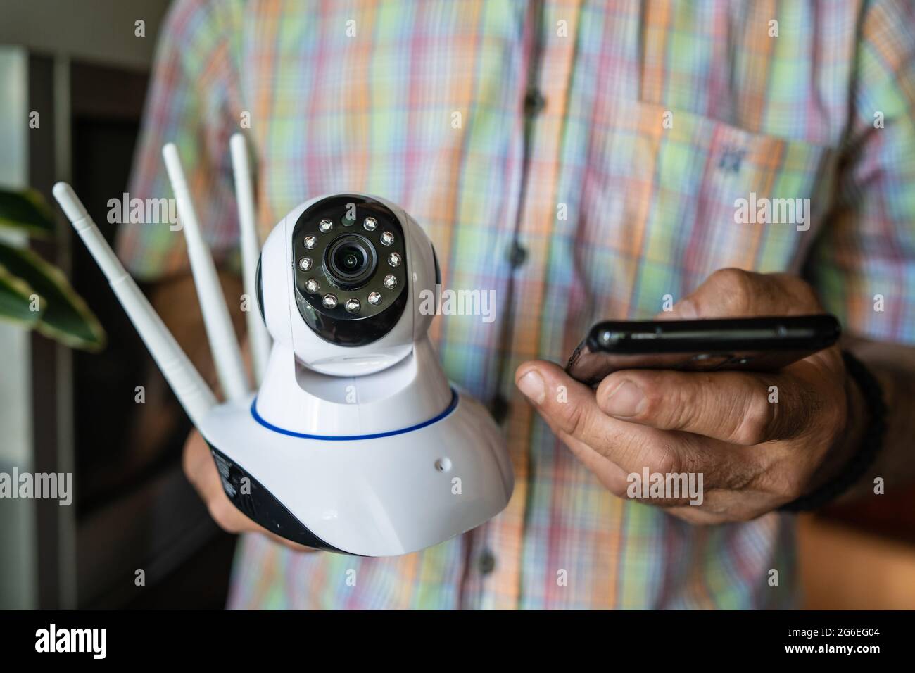 Close up on midsection of unknown man holding home security surveillance camera and mobile phone trying to install an app front view copy space Stock Photo
