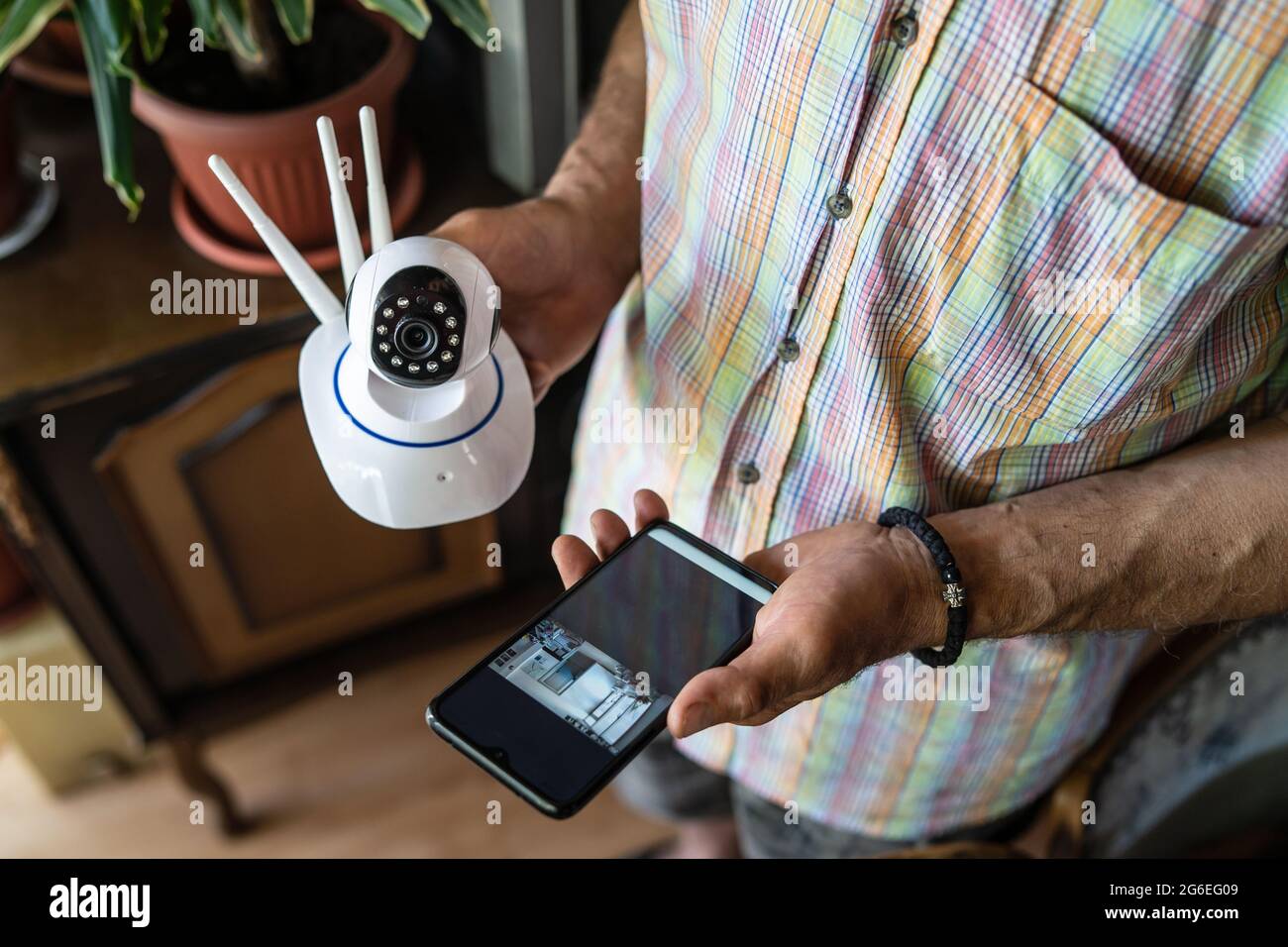 Close up on midsection of unknown man holding home security surveillance camera and mobile phone trying to install an app top view copy space Stock Photo