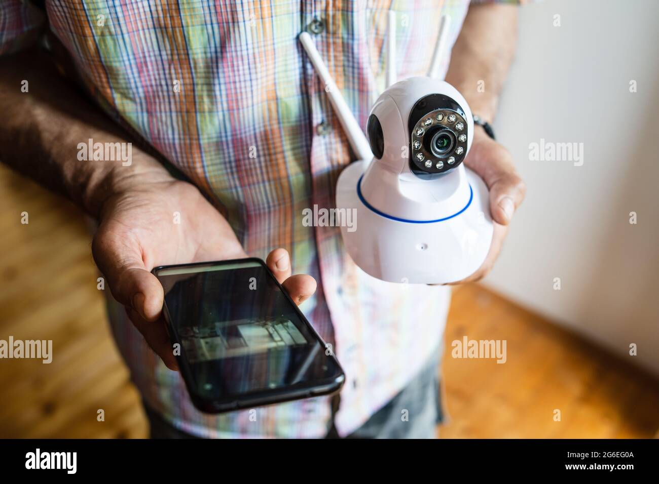 Close up on midsection of unknown man holding home security surveillance camera and mobile phone trying to install an app top view copy space Stock Photo