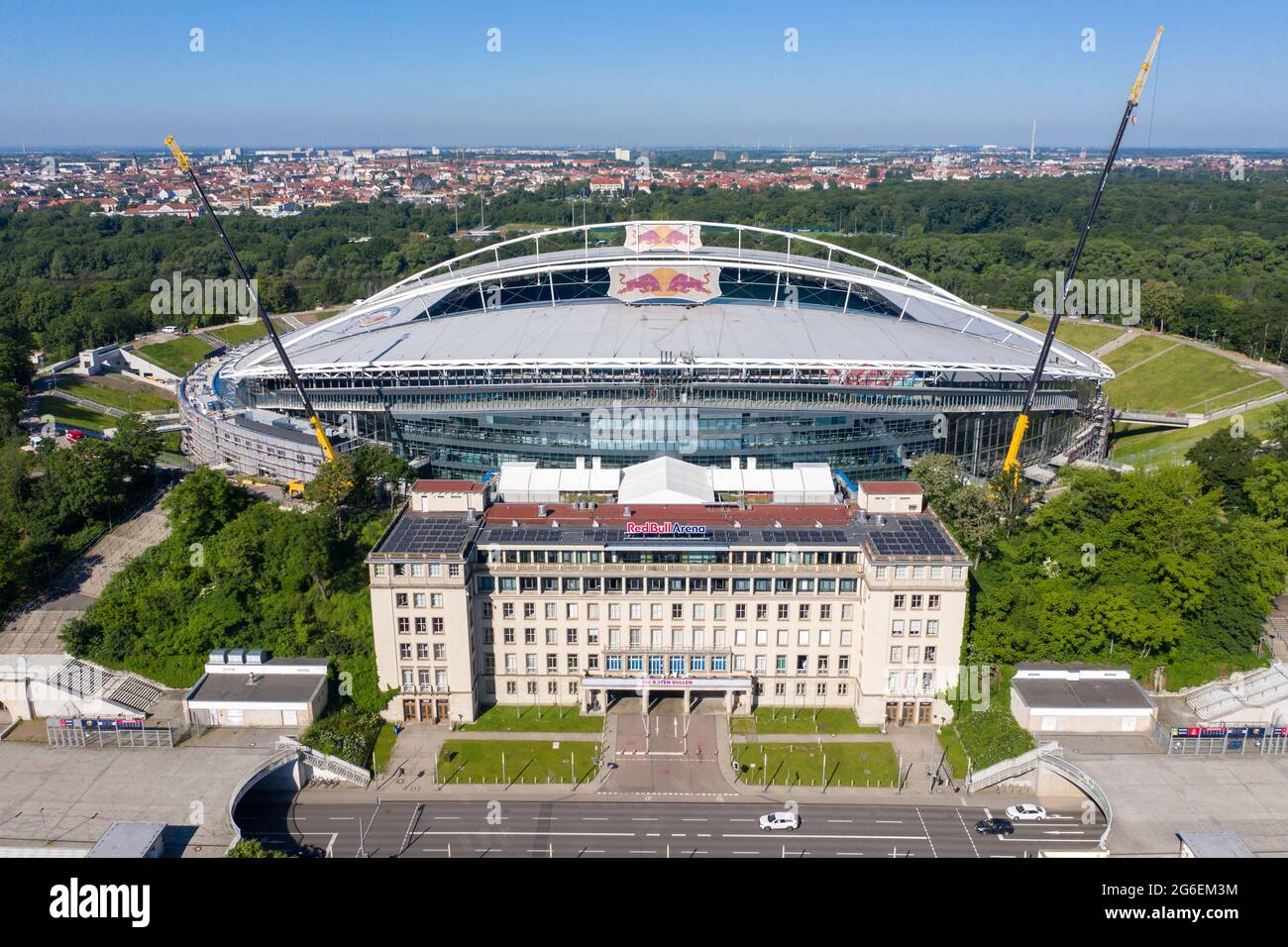 14 June 2021, Saxony, Leipzig: Football: Bundesliga, RB Leipzig. Two cranes are at the Red Bull Arena. The home ground of the Rasenballers is being rebuilt. The spectator capacity will increase from 42,558 to 47,069 in standing and seated areas. The outside of the stadium is enclosed with a soundproof facade. The embankment of the former Zentralstadion, which encompasses the arena, was cut open behind the historic bell tower to make room for a new entrance. RB Leipzig is investing a good 60 million euros in the conversion by 2022. (Aerial view with drone) Photo: Jan Woitas/dpa-Zentralbild/dpa Stock Photo