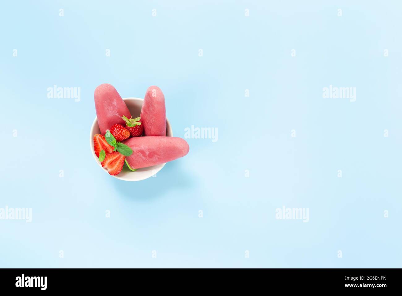 Top view on bowl with fruity pink frozen sorbet ice-cream on plastic stick with strawberry, mint on blue background. Frozen mixed fruits with yogurt i Stock Photo