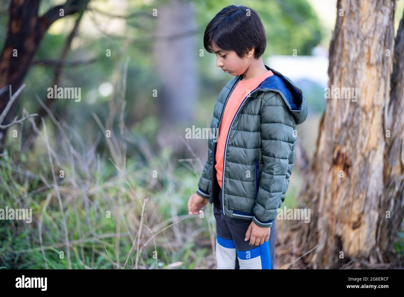 Lonely Young boy standing touching the grass. Portrait of child outdoors in natural light. Natural environment, loneliness. Stock Photo