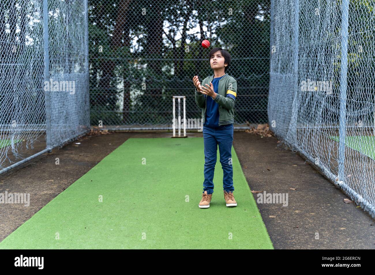Young boy playing with cricket ball at cricket pitch under nets. Stock Photo