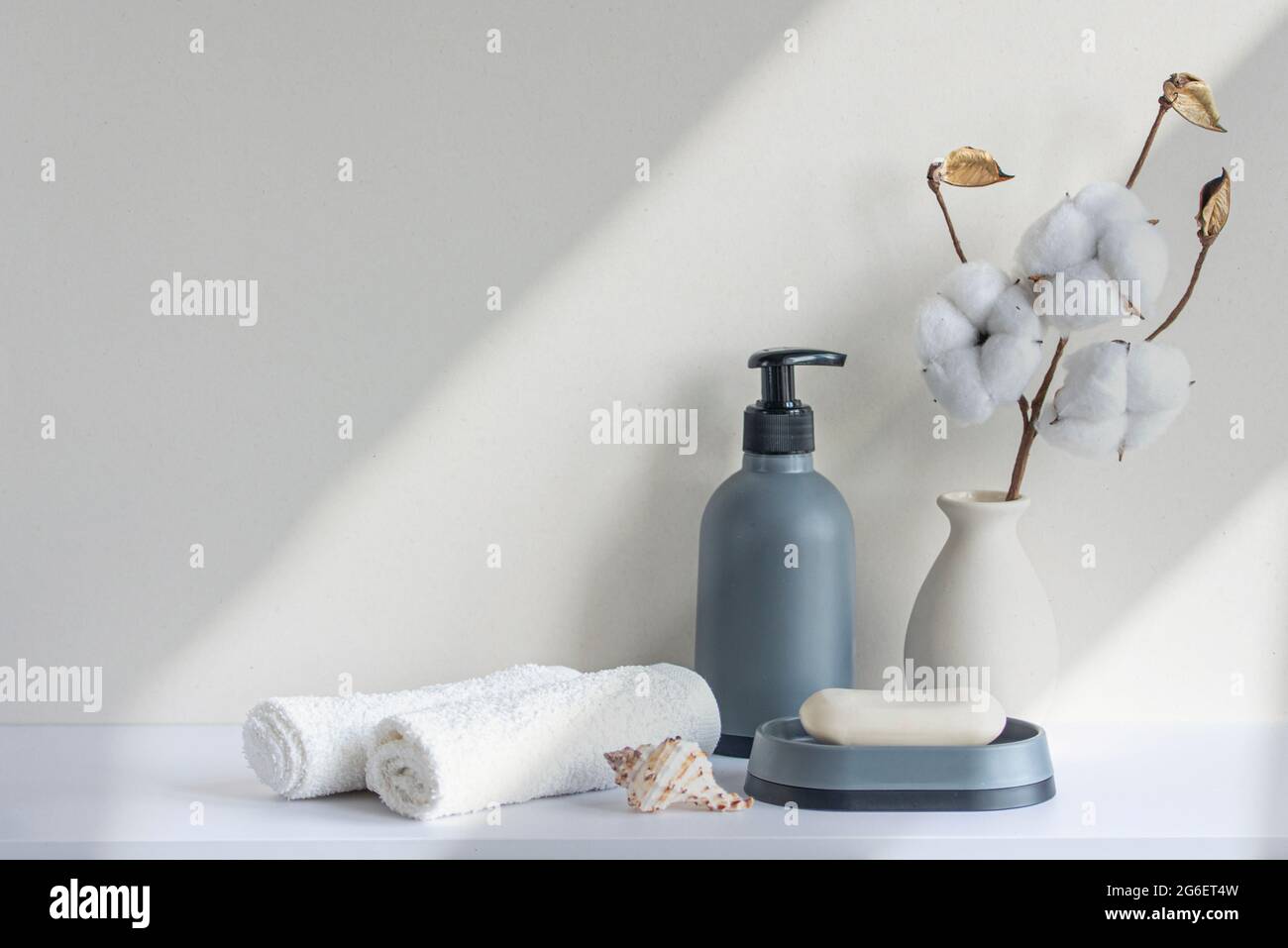 Bathroom interior in beige pastel tone. White shelf in bathroom with towels, soap, shampoo bottle, houseplant. Mockup with space for text. Minimal com Stock Photo