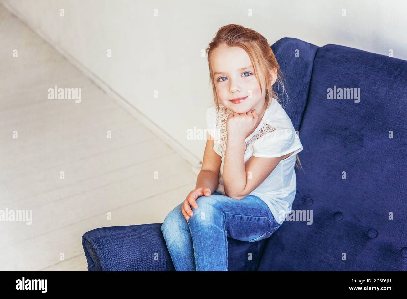 Sweet little girl in jeans and white T-shirt sitting on modern cozy ...