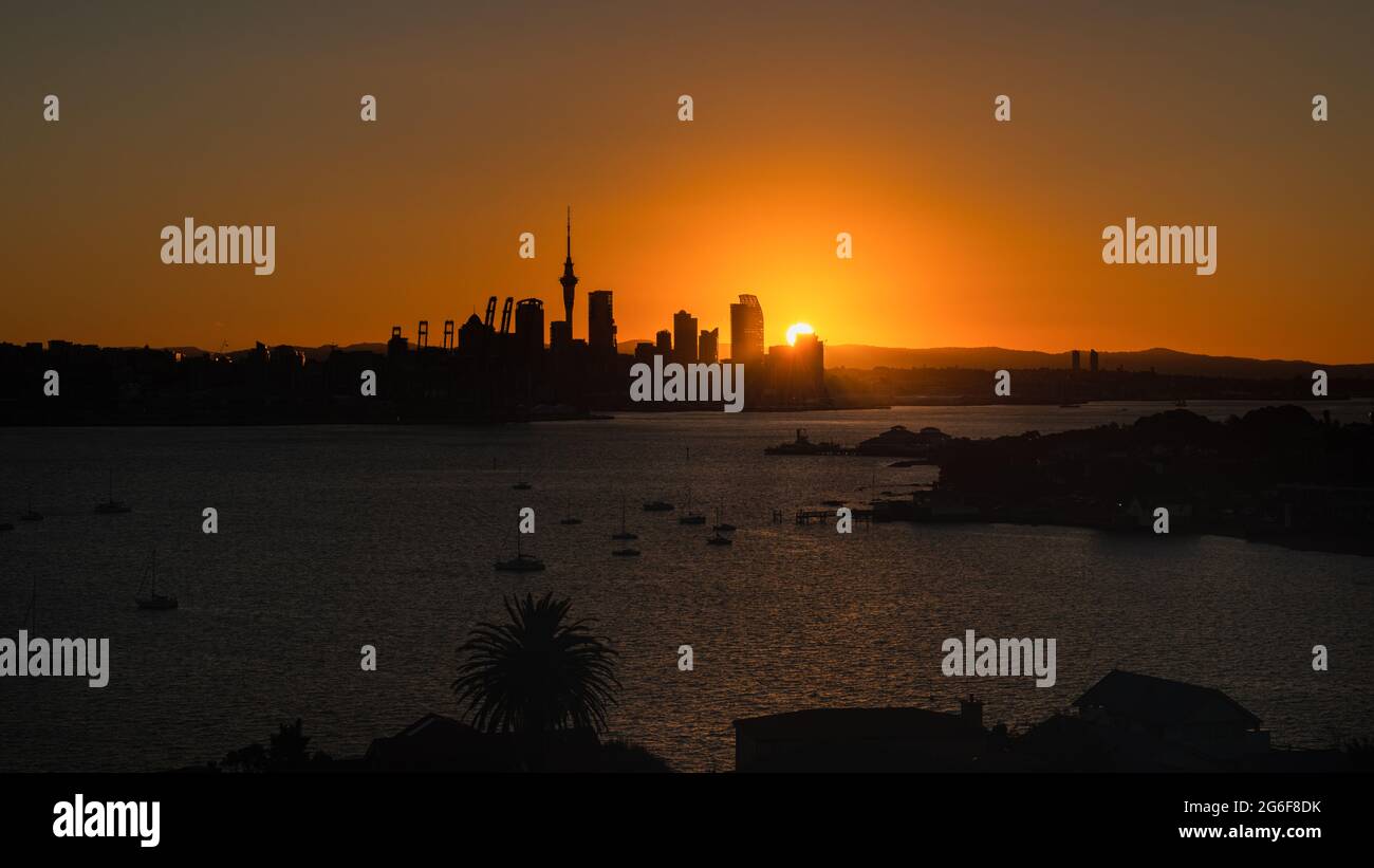 Auckland city in silhouette with the sun setting behind the tall buildings Stock Photo