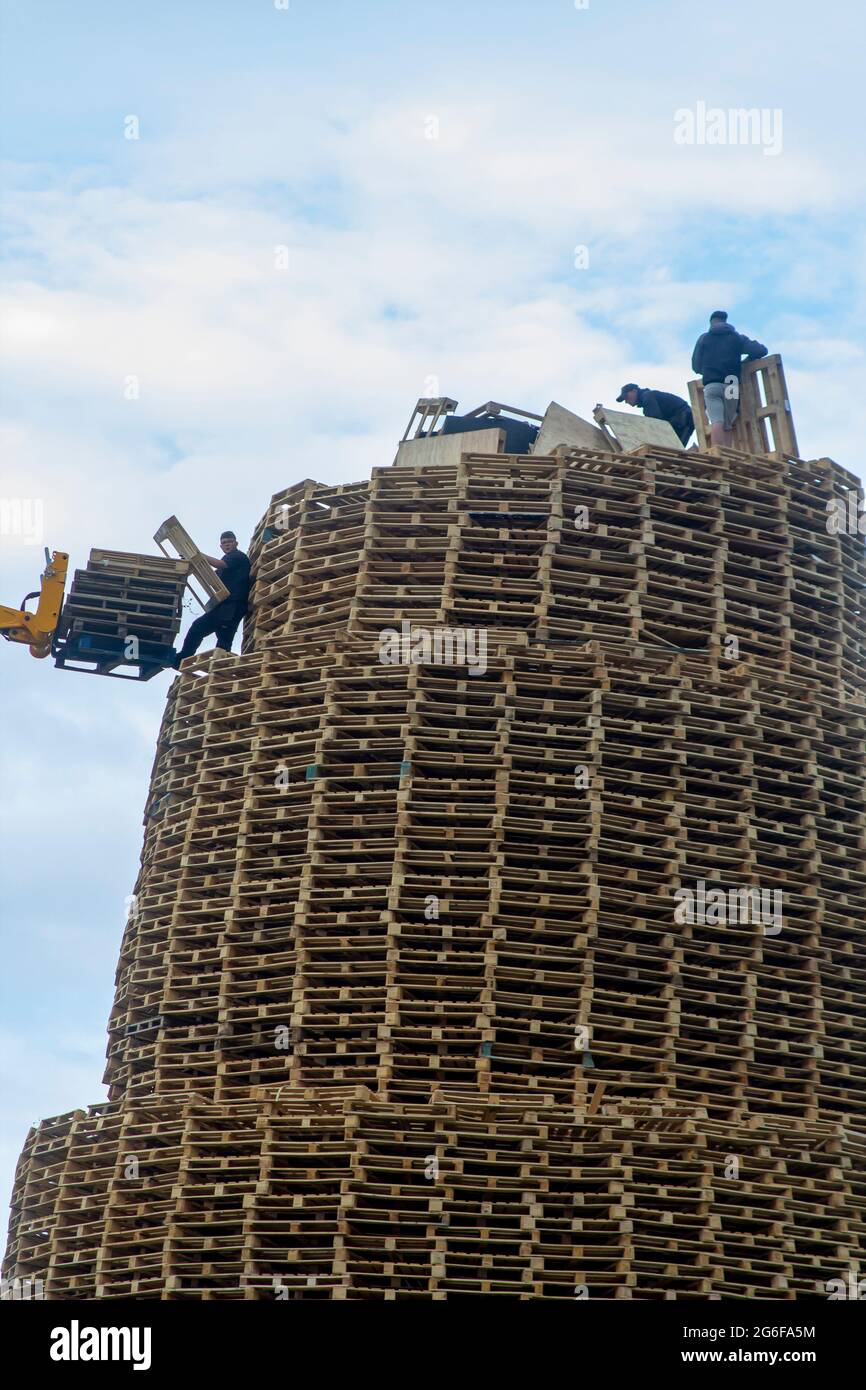 4 July 2021 Youths on top of the very tall bonfire made from thousands of wooden industrial pallets as they prepare for the 12th of July celebrations Stock Photo