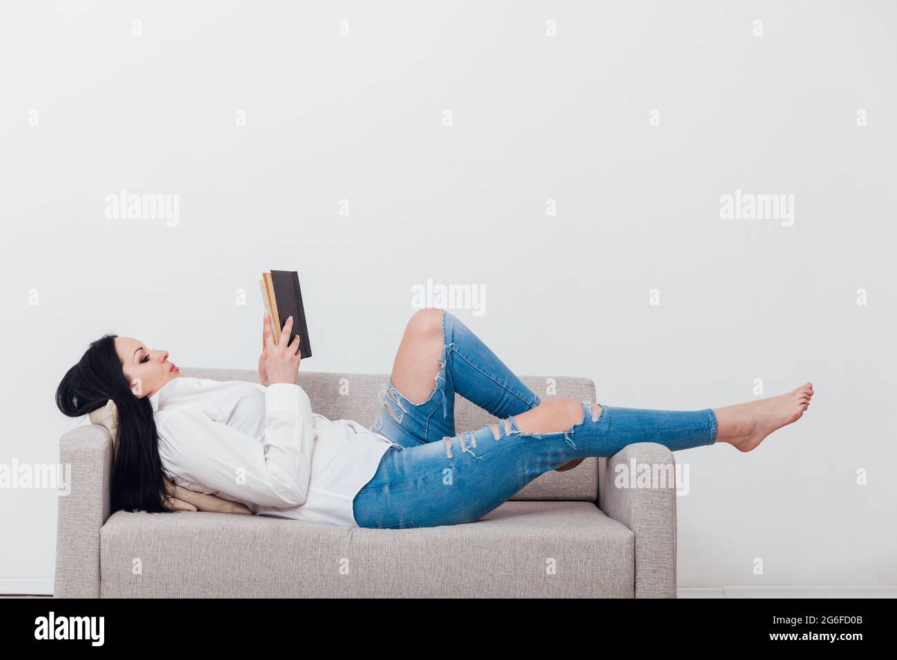 Beautiful brunette woman reads a book at home on the couch Stock Photo