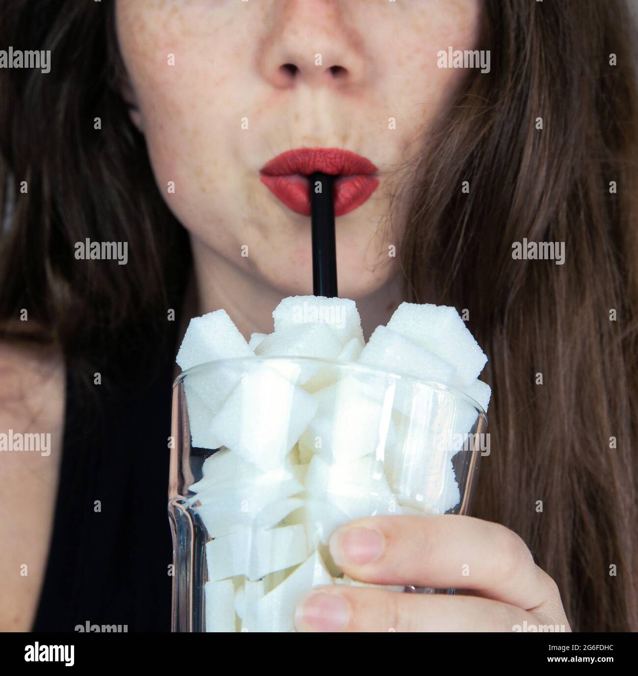 Portrait of young woman drinking with a black colored straw from a glass filled with sugar cubes Junk food, unhealthy diet, too much sugar on drinks, Stock Photo