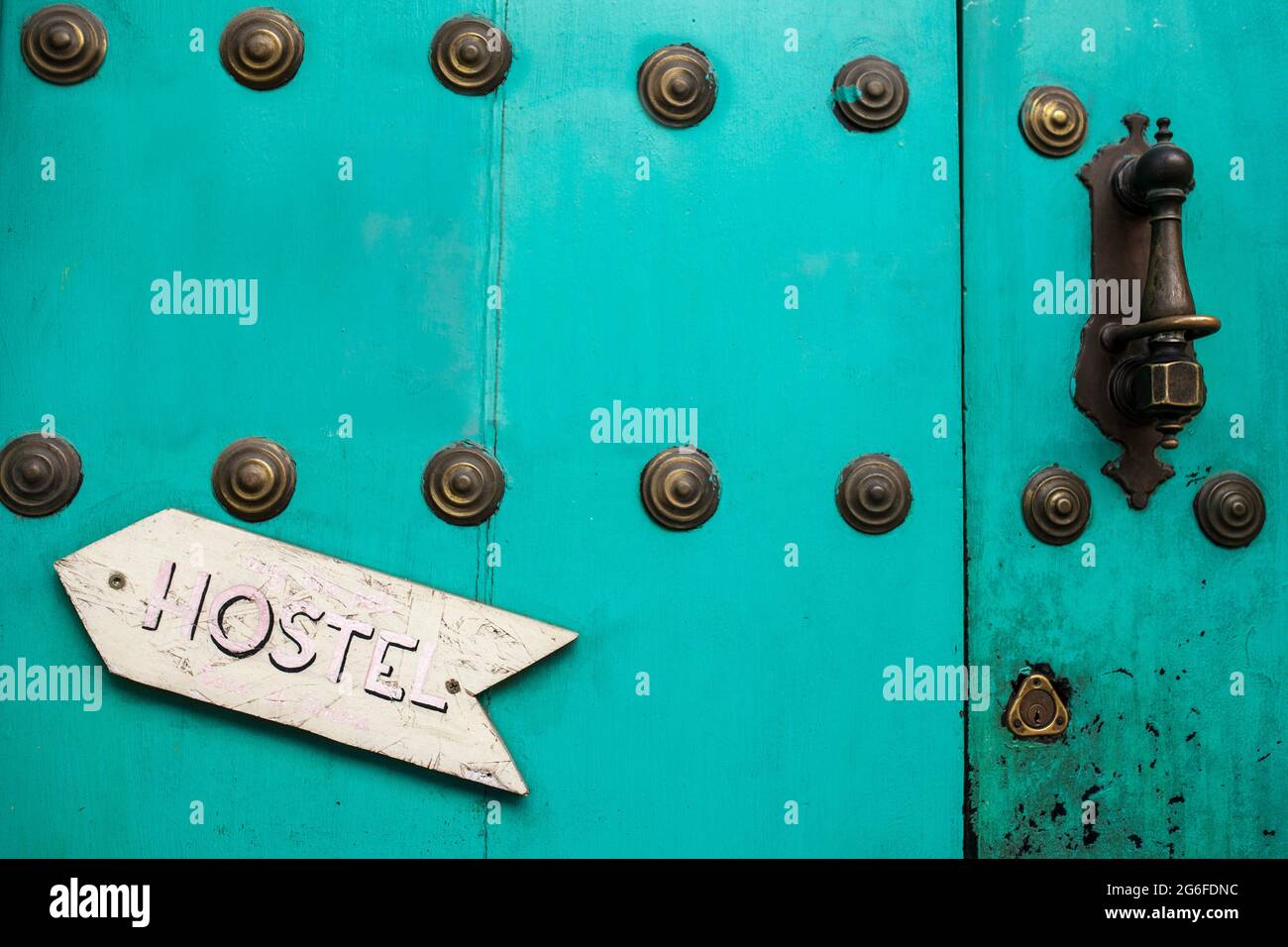 Old rusty blue door with Hostel arrow sign pointing the doorknocker. Cheap and fun youth hostel concept. Stock Photo