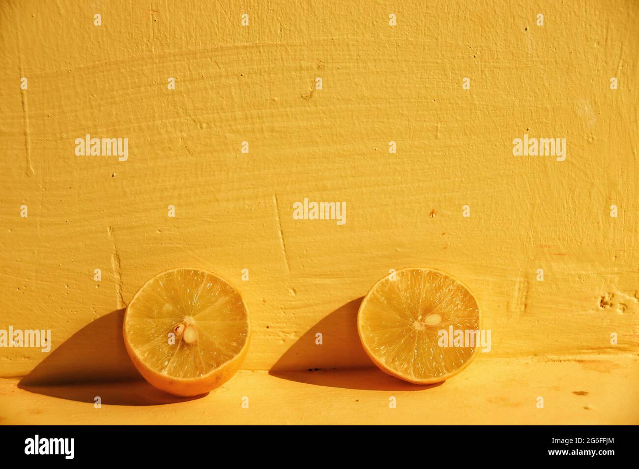 Two slices of lemons against a yellow colored wall Stock Photo