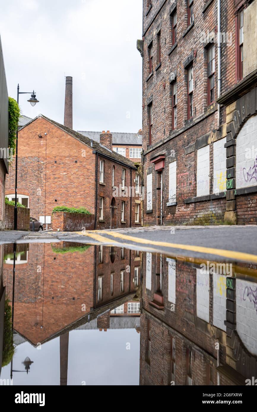 Old industrial back street with cobbled lane, cottages and old factory buildings reflected like a mirror image in flood water on road.  No people. Stock Photo