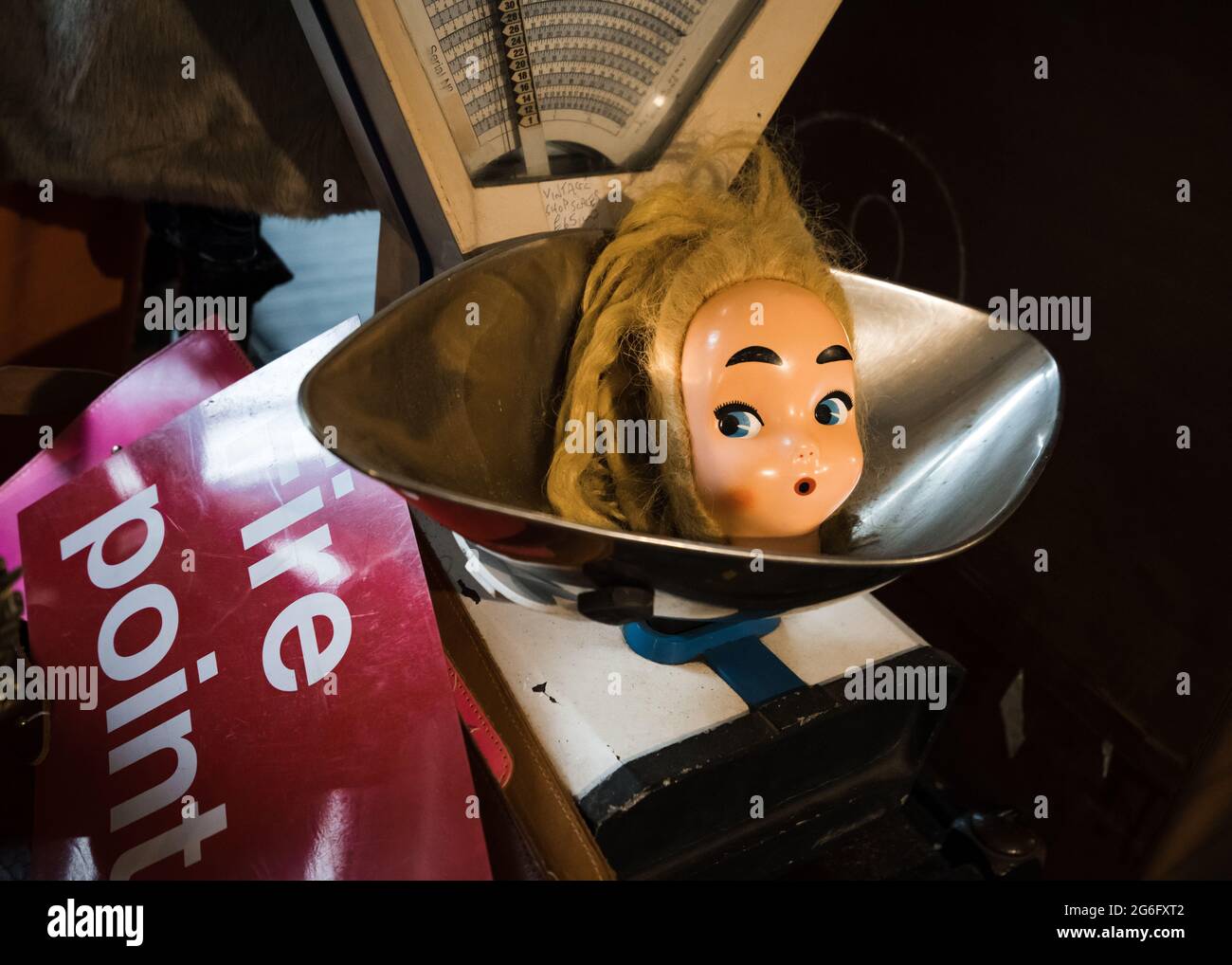 Creepy dolls head in vintage weighing scales with surprised look on face raised eyebrows decapitated doll. Old fashioned scales. Strange face and dark Stock Photo