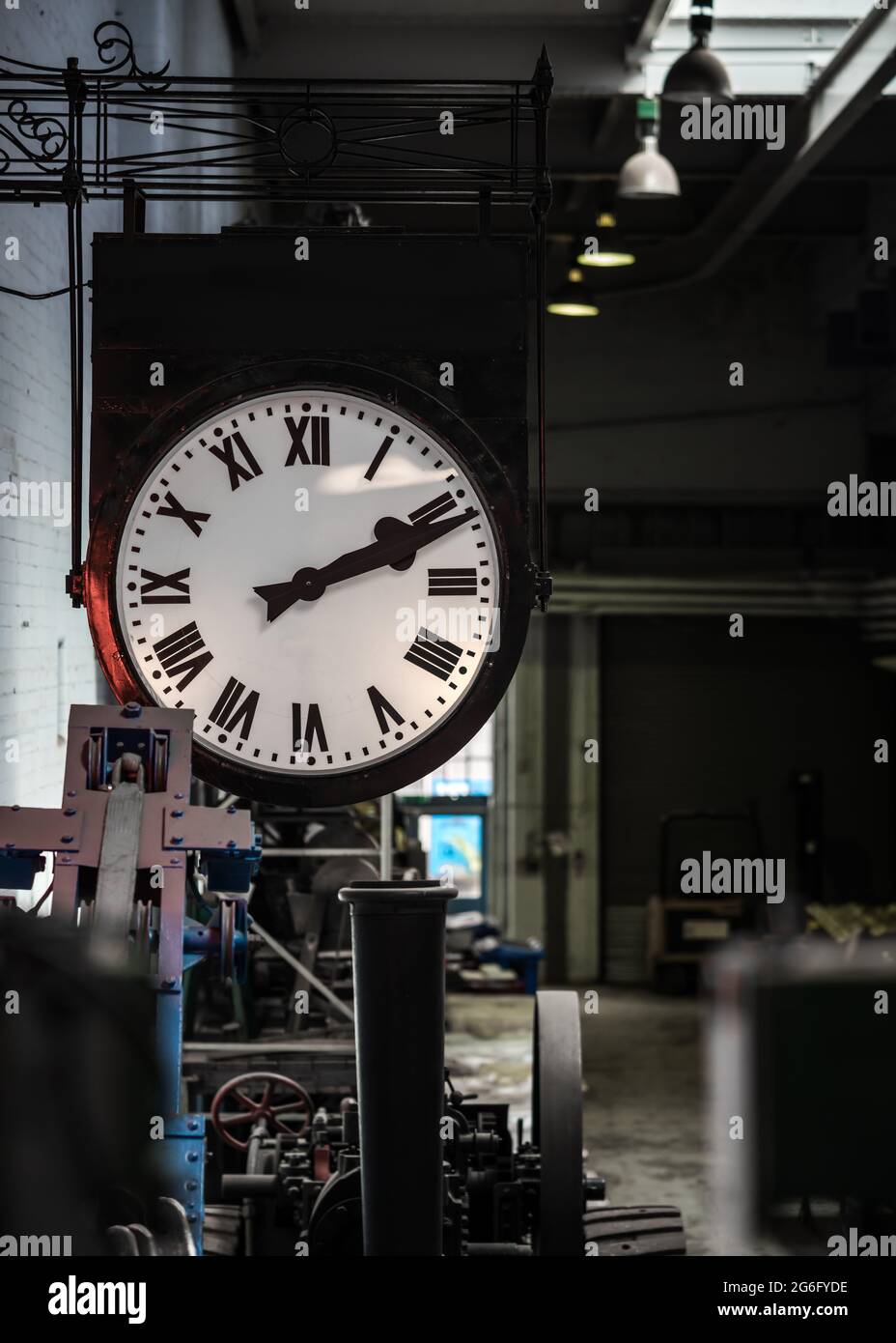 Old fashioned vintage big industry factory clock hanging with roman numerals in abandoned building no workers. Industrial workshop clocking off time Stock Photo