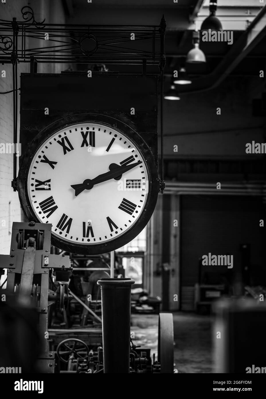 Old fashioned vintage big industry factory clock hanging with roman numerals in abandoned building no workers. Industrial workshop clocking off time Stock Photo