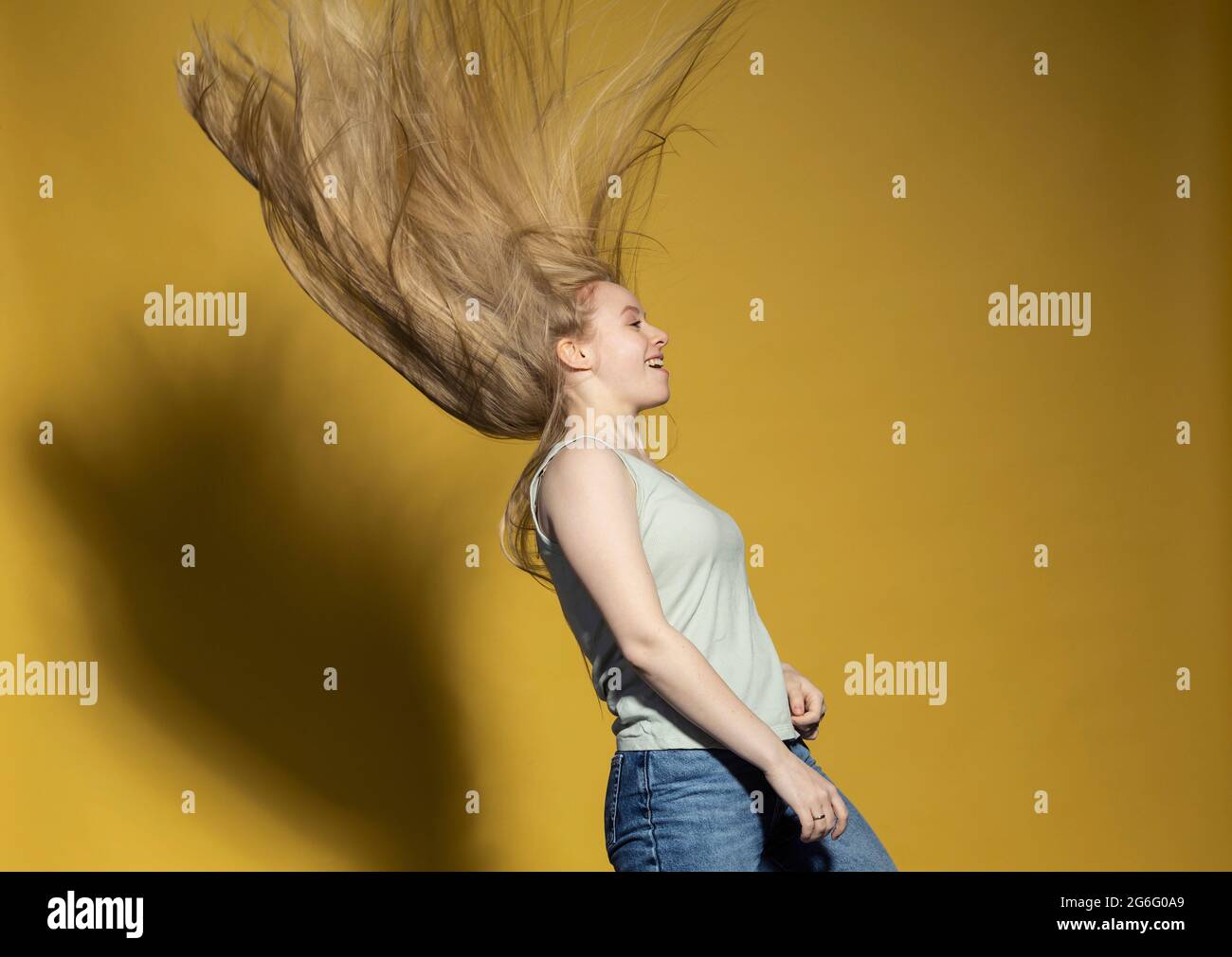 Carefree young woman flipping long blonde hair against yellow background Stock Photo