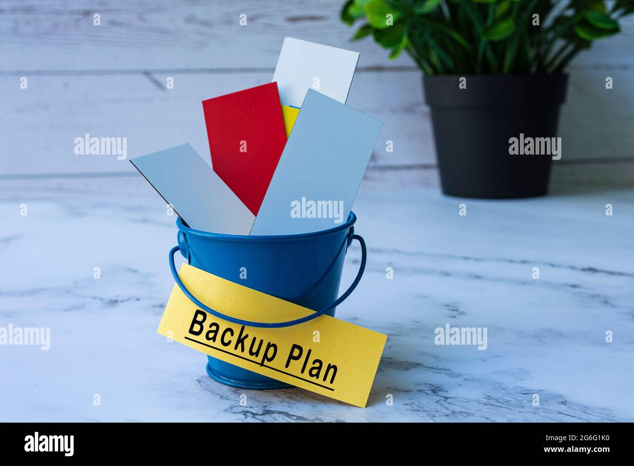 Text on yellow paper with colorful paper inside of a blue bucket. Backup plan Stock Photo