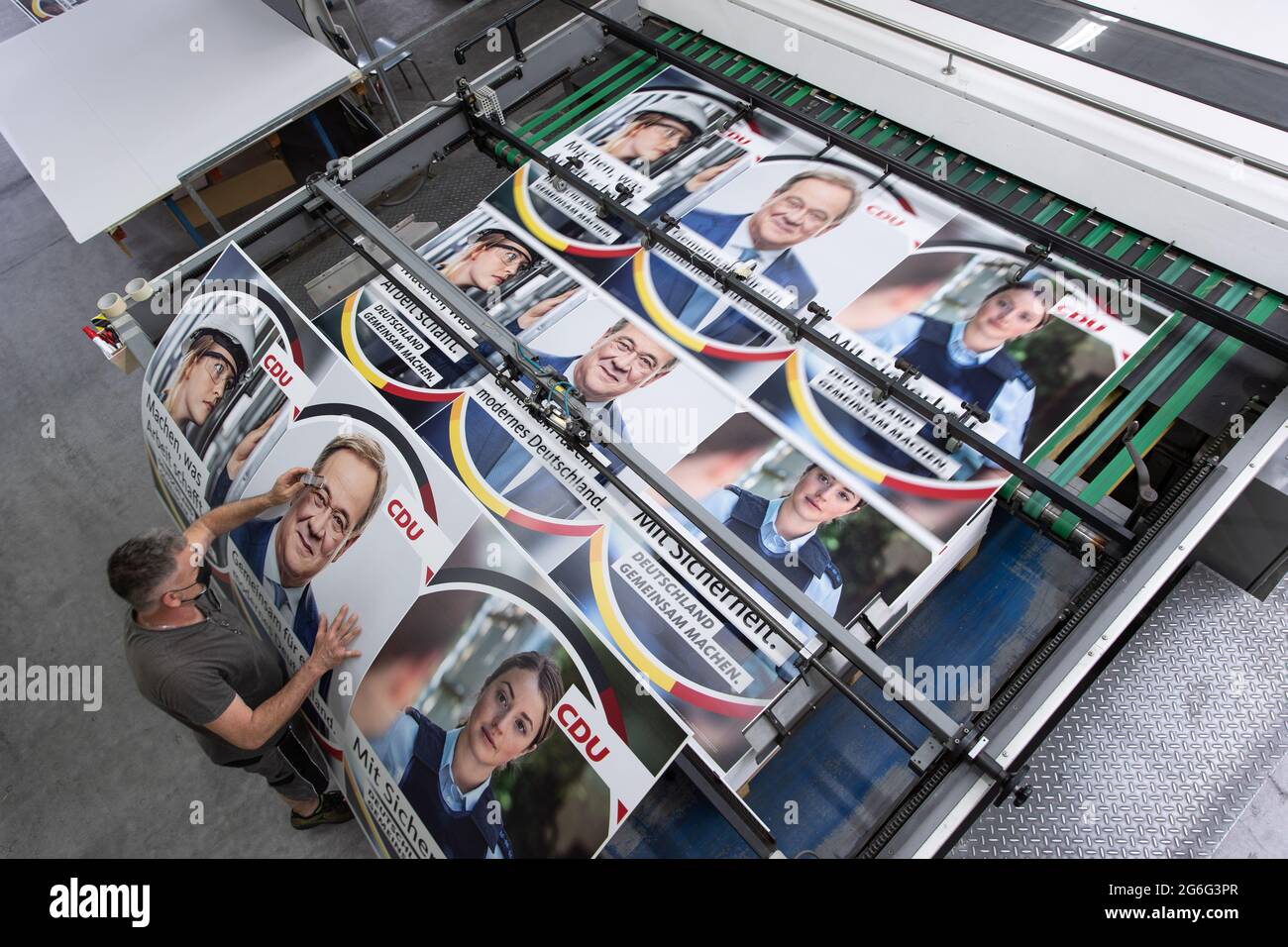 PRODUCTION - 29 June 2021, North Rhine-Westphalia, Holte-Stukenbrock: Printer Marc Berenbrinker a magnifying glass to a CDU election poster with a picture of party leader and German Chancellor