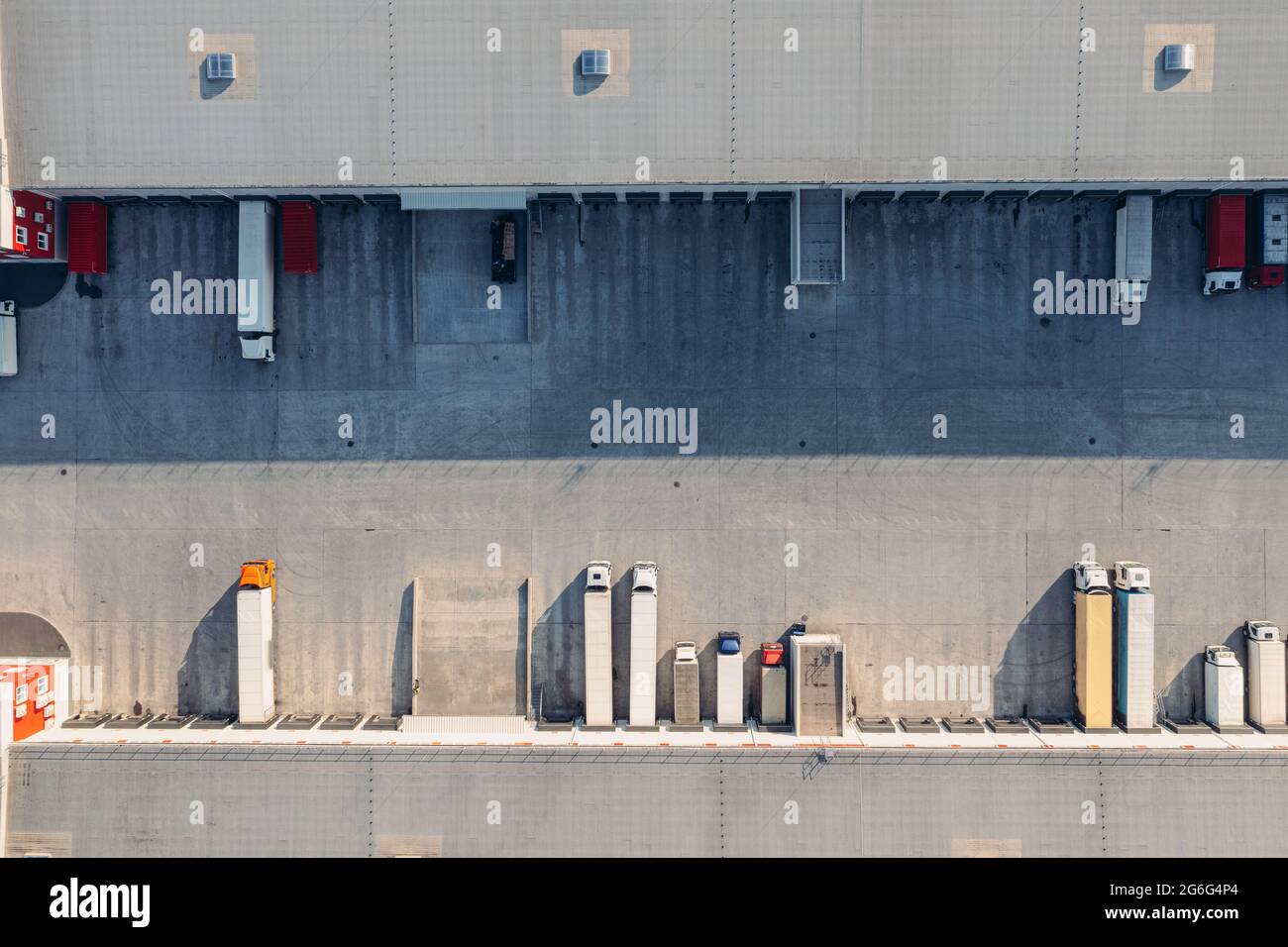 Trucks with trailers wait for the loading of goods for transportation in the loading warehouse. Aerial top view drone shot. A large transit cargo terminal with trucks and trailers. Stock Photo