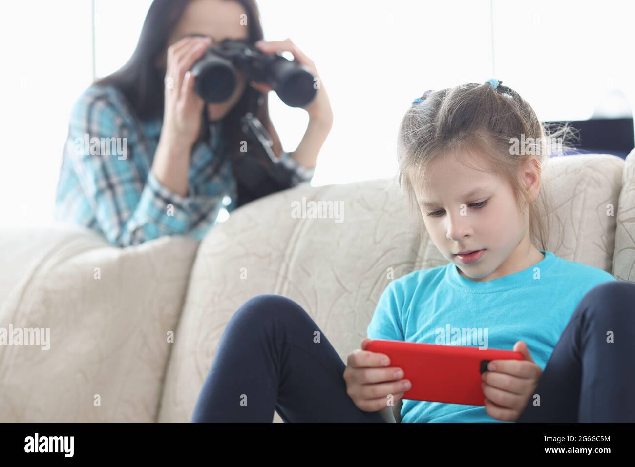 Mom controls her daughter with phone through binoculars Stock Photo