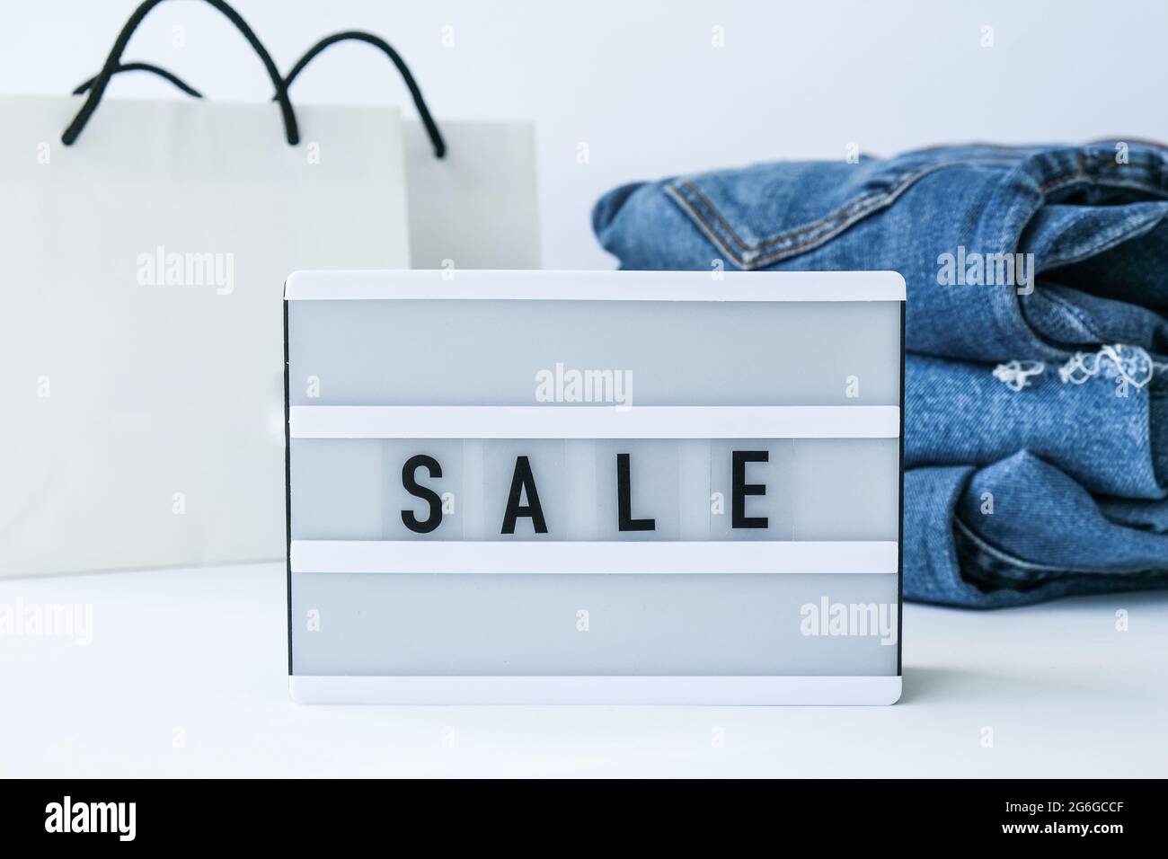 Light board with text SALE with paper shopping bags, jeans clothes. Big Sale online shopping concept. Promotion advertising. Holiday Stock Photo