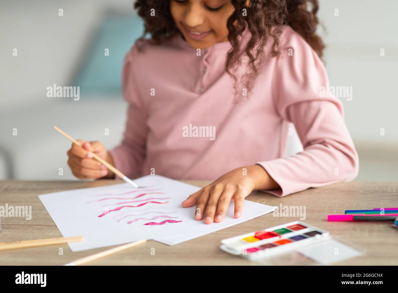 Inspired african american teen girl with brush and palette painting, enjoying her new hobby, sitting at desk at home Stock Photo