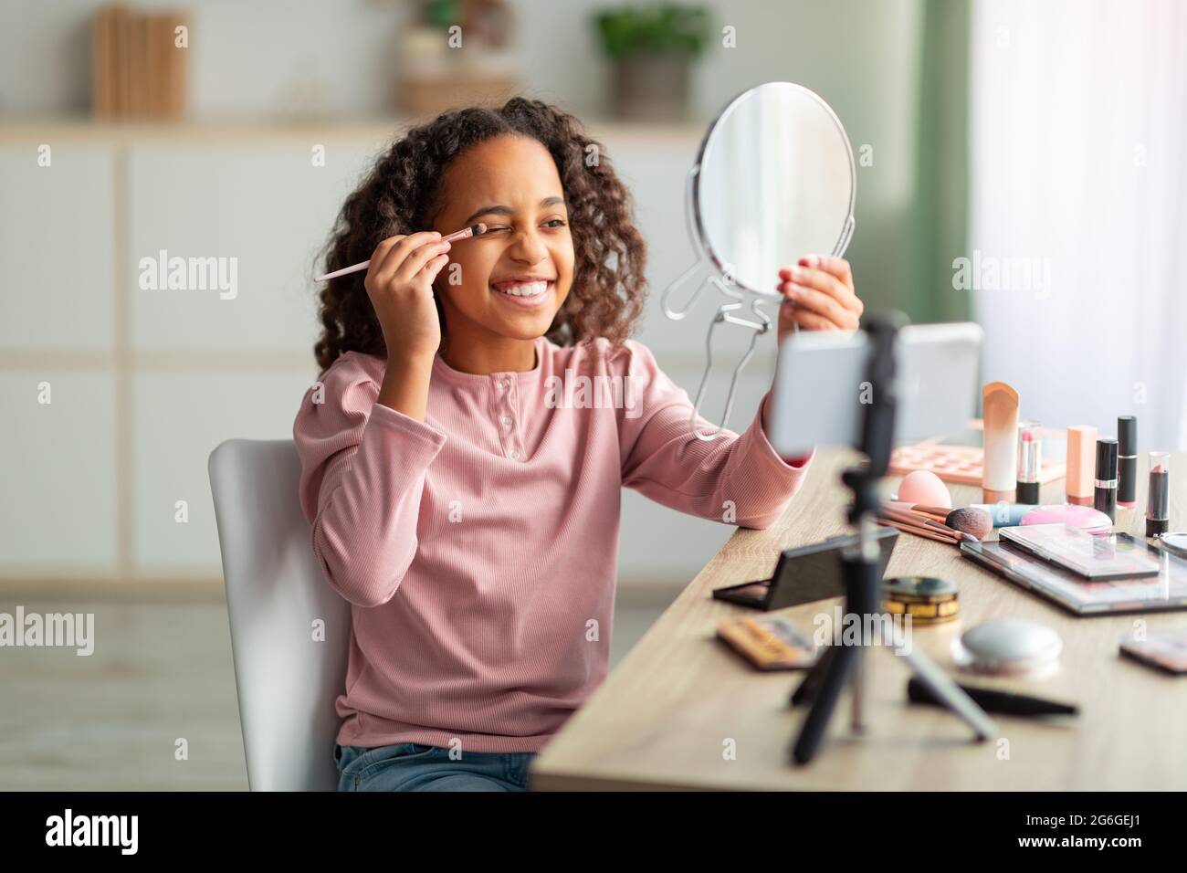 Beauty blog for teenagers. Joyful african american girl applying eyeshadows and recording cosmetics product review Stock Photo