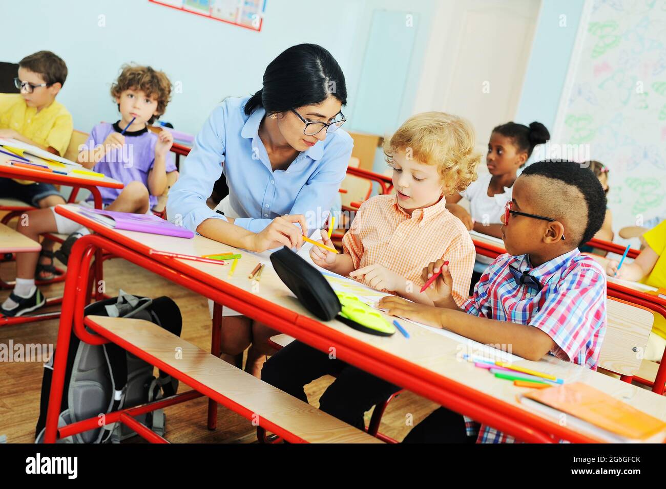 young woman teacher helps children to do the job in the classroom in