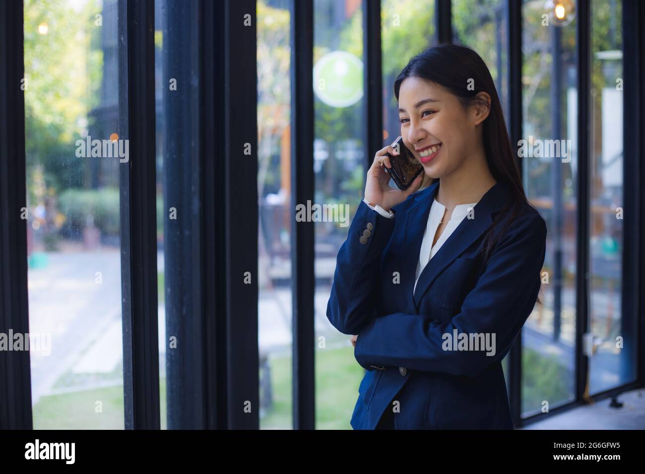 Confidential business Asian young woman cross armed and talk on phone in office, smart and cheerful businesswoman or manager Stock Photo