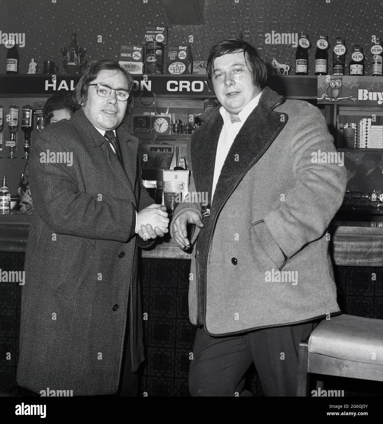 1970s, historical, two second hand car dealers in their coats, standing together in a bar having a lunchtime drink, Croydon, England, UK. Classic drinks of the day can be seen; Ind Coope Light Ale, Skol Lager and a party can of Double Diamond for 81 pence! Stock Photo
