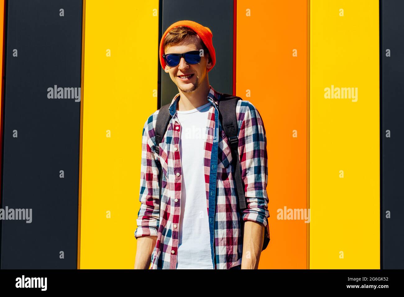 Young smiling hipster man in a hat and sunglasses, in stylish clothes with a briefcase, posing on a bright colored background Stock Photo