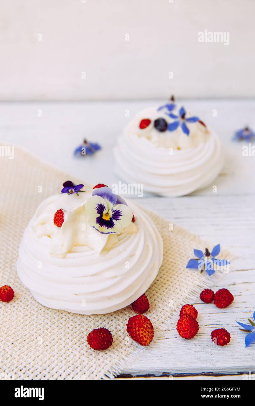 Small meringue cakes, decorated with whipped cream, fresh berries and real life edible flower