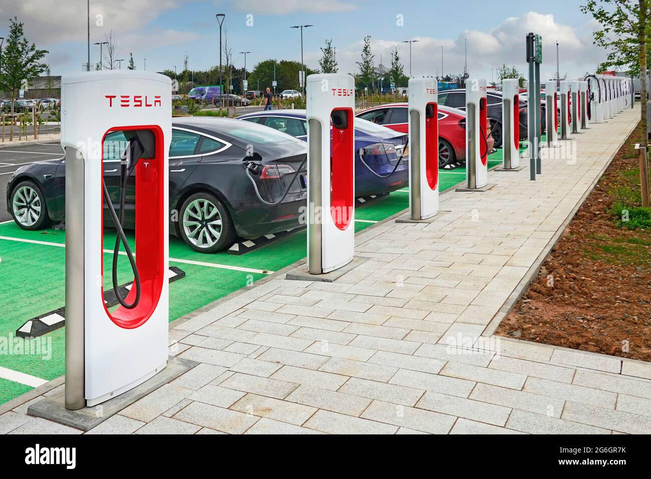 Impact of climate change concerns brings new infrastructure installation electric car charging points & row of connected cars & cables Rugby Moto UK Stock Photo