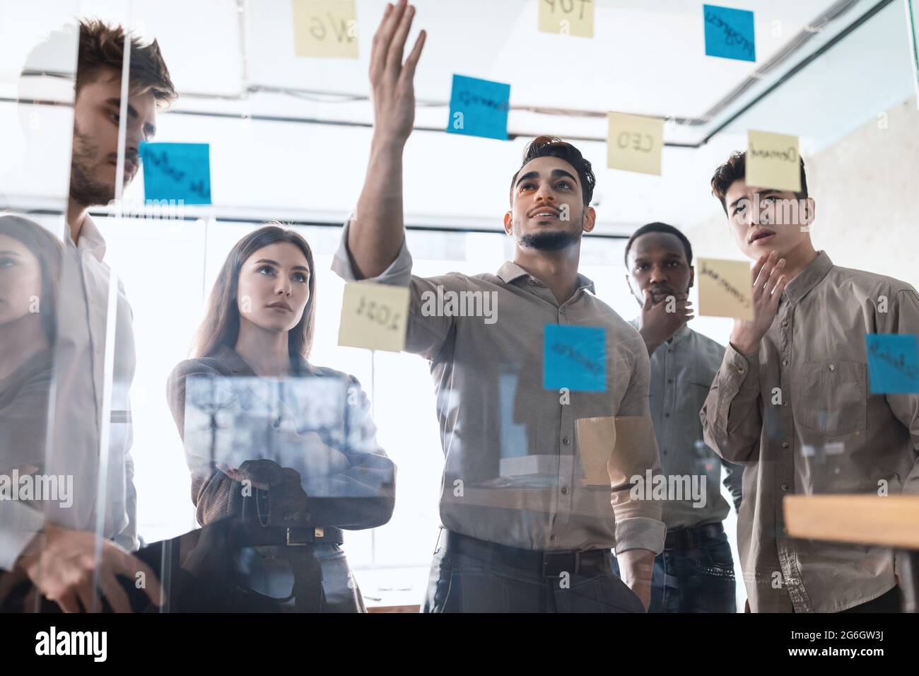 Diverse colleagues brainstorming using sticky notes on glass wall Stock Photo