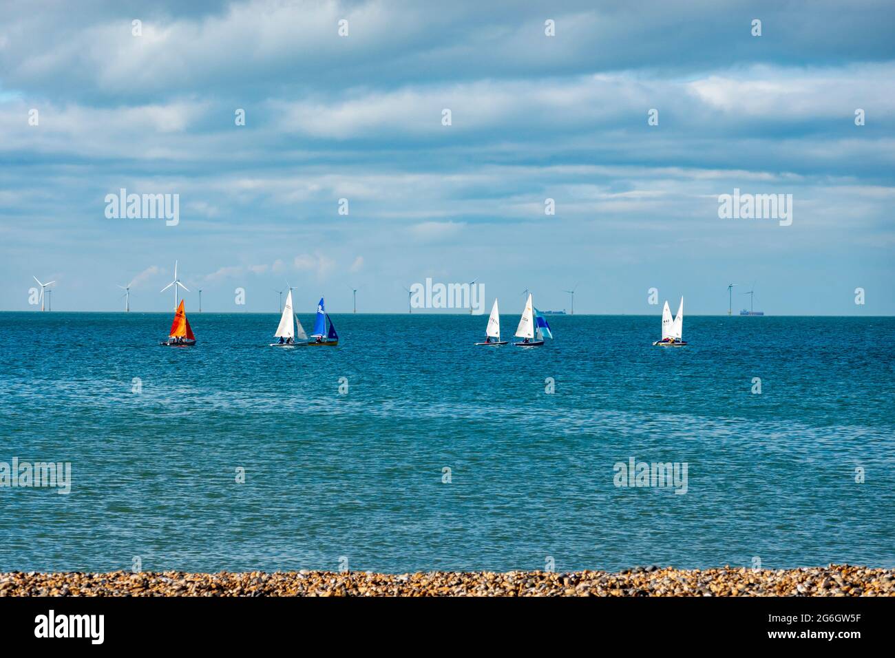 Sailing dinghies racing off the beach at Hampton, Herne Bay, Kent. In the distance are the wind turbines of the Thames wind Array, UK Stock Photo