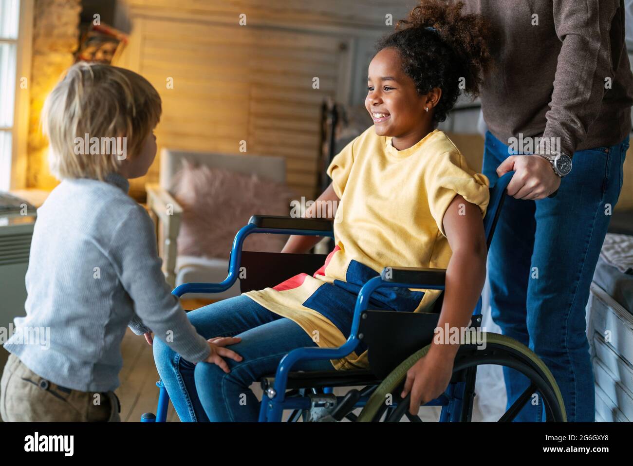 Happy multiethnic family. Smiling little girl with disability in wheelchair at home Stock Photo