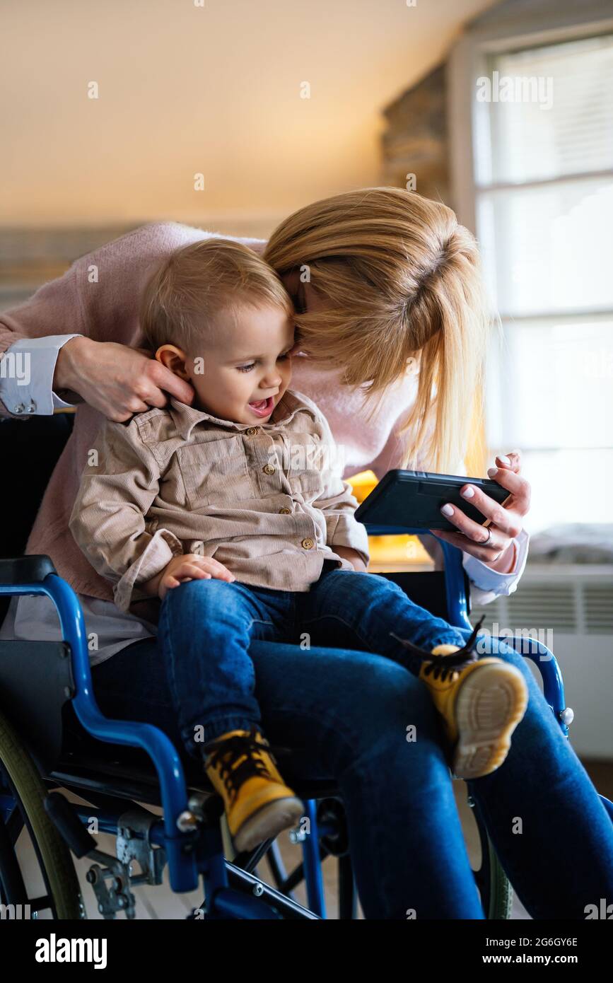 Happy mother in wheelchair with child using digital tablet at home. People family happiness concept. Stock Photo