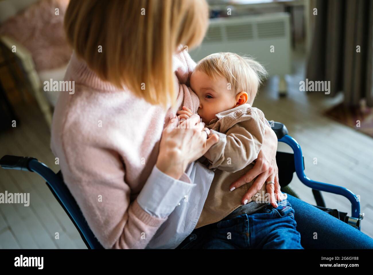 Young mother with disability in wheelchair breast feeding her child at home Stock Photo