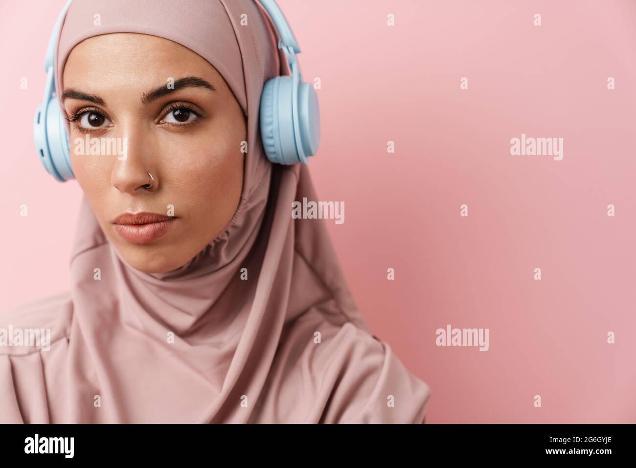 A portrait of the muslim woman wearing pink hijab with headphones ...