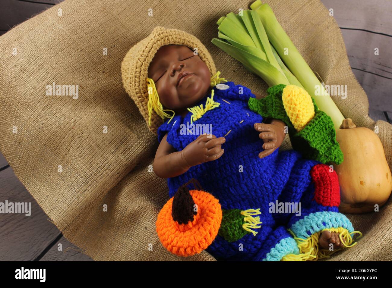African American baby in blue dungarees surrounded by autumn vegetables. Harvest festival concept represented by a reborn doll Stock Photo