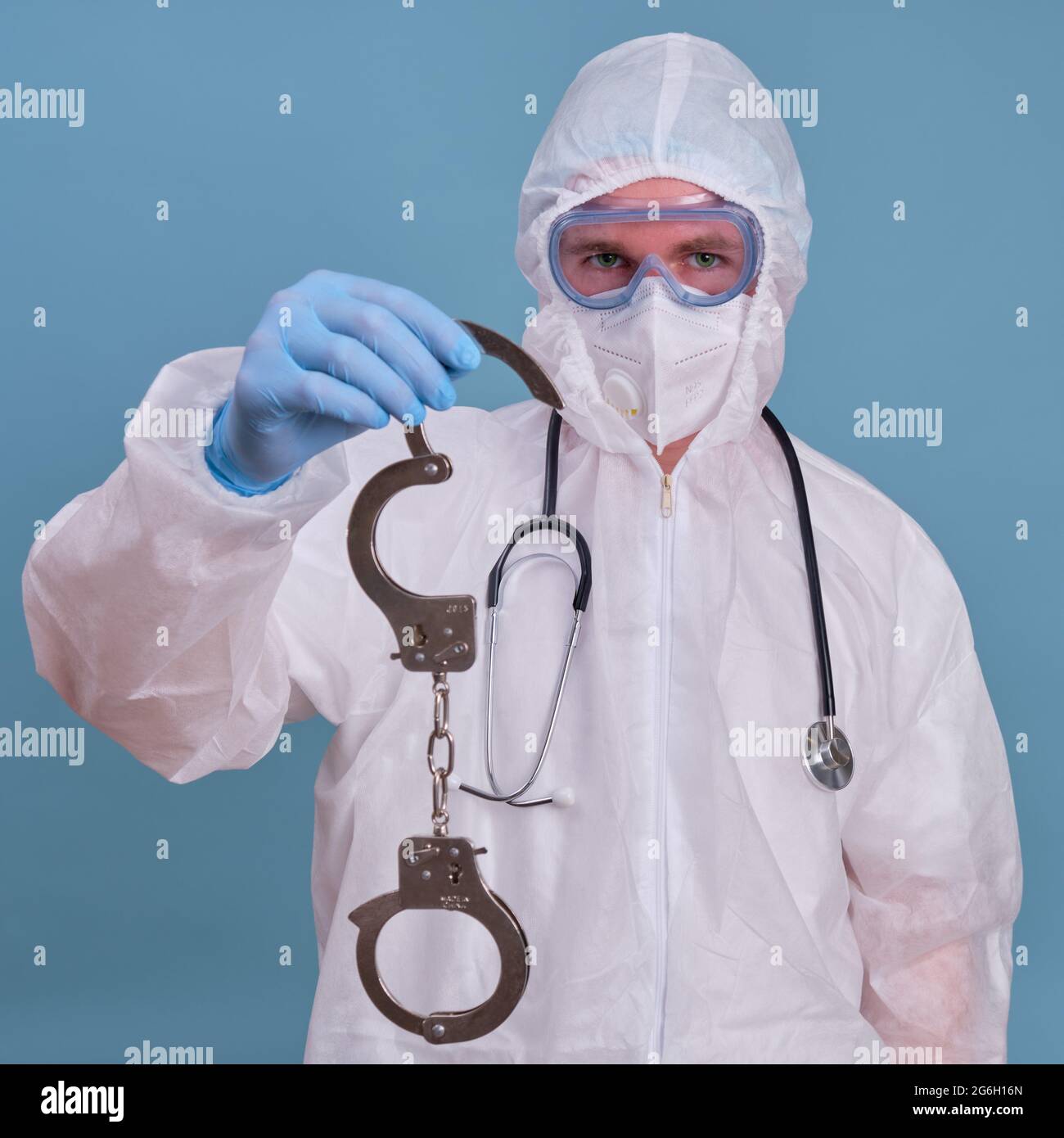 A doctor in a white uniform wearing a medical face mask with handcuffs in his hands Stock Photo