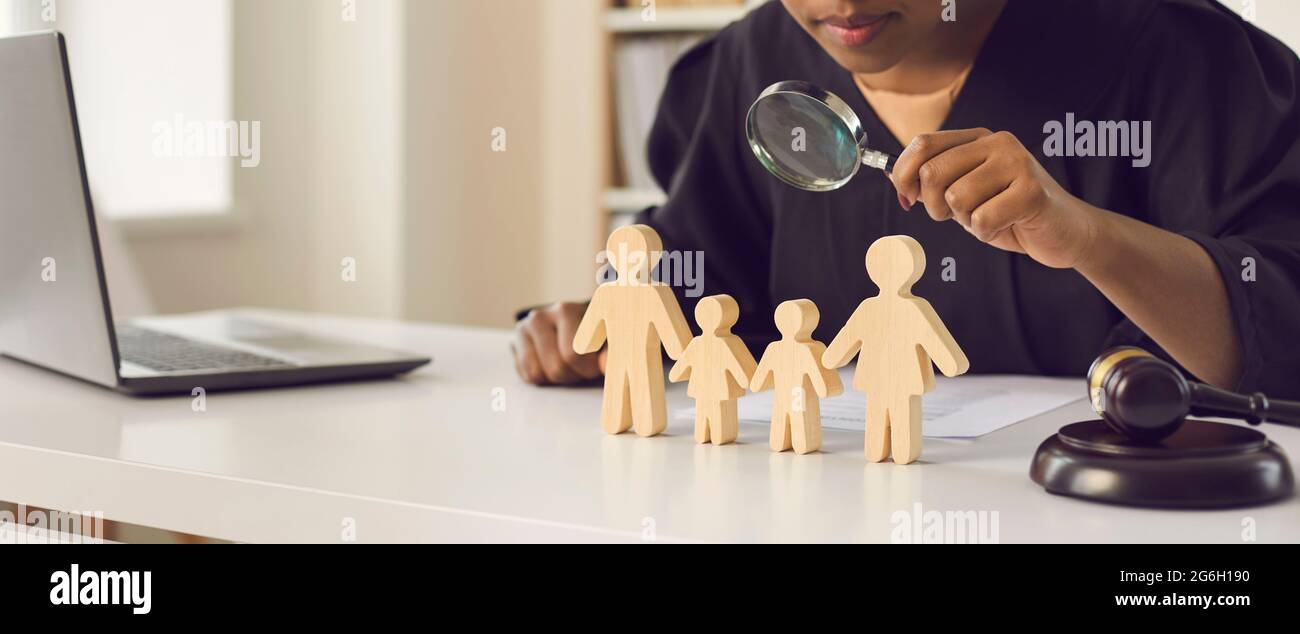 Judge with magnifying glass looking at wooden family figures standing on the table Stock Photo
