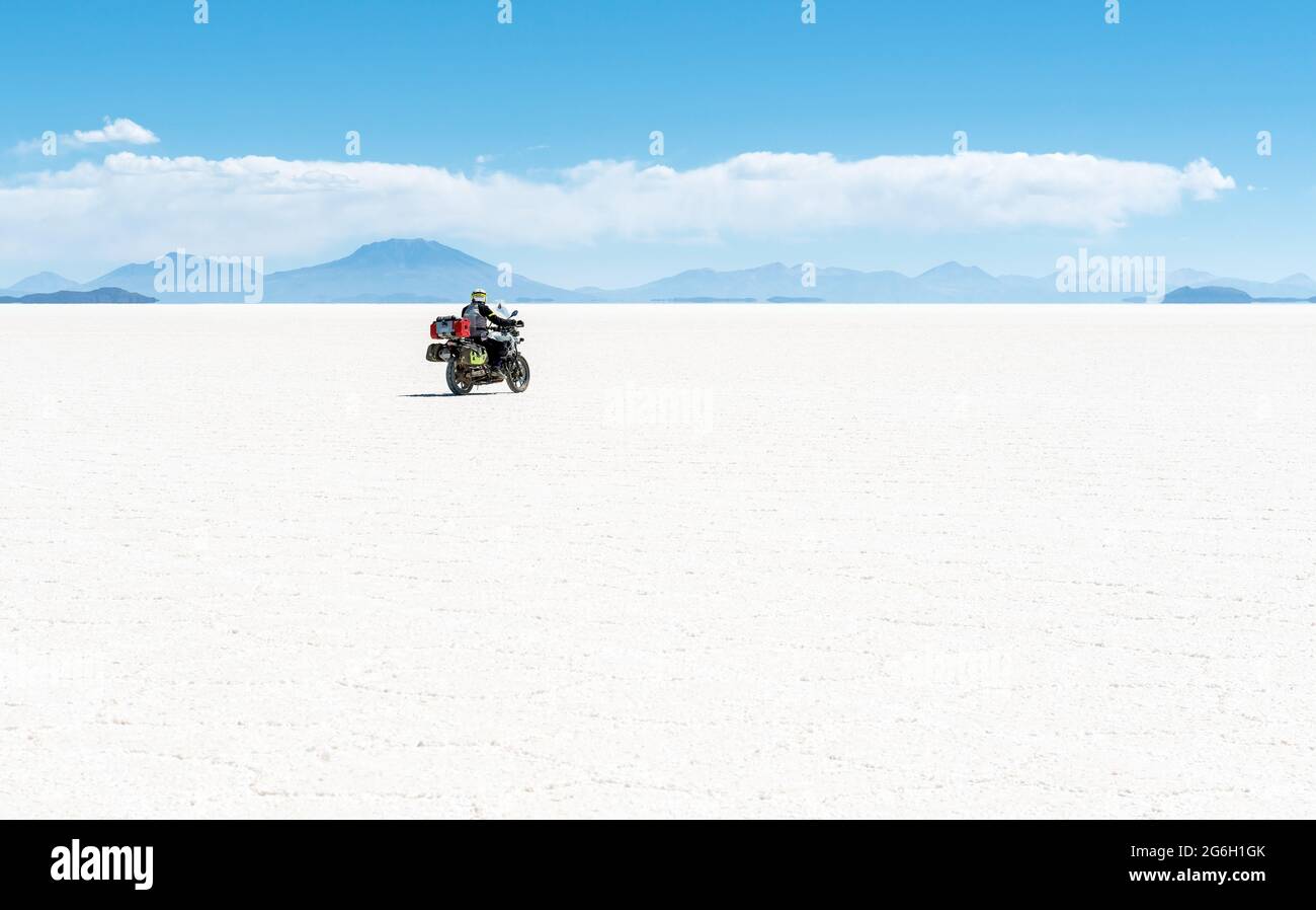 Motorcyclist riding through Uyuni salt flat desert, Bolivia. Adventure road trip with motorbike. Stock Photo