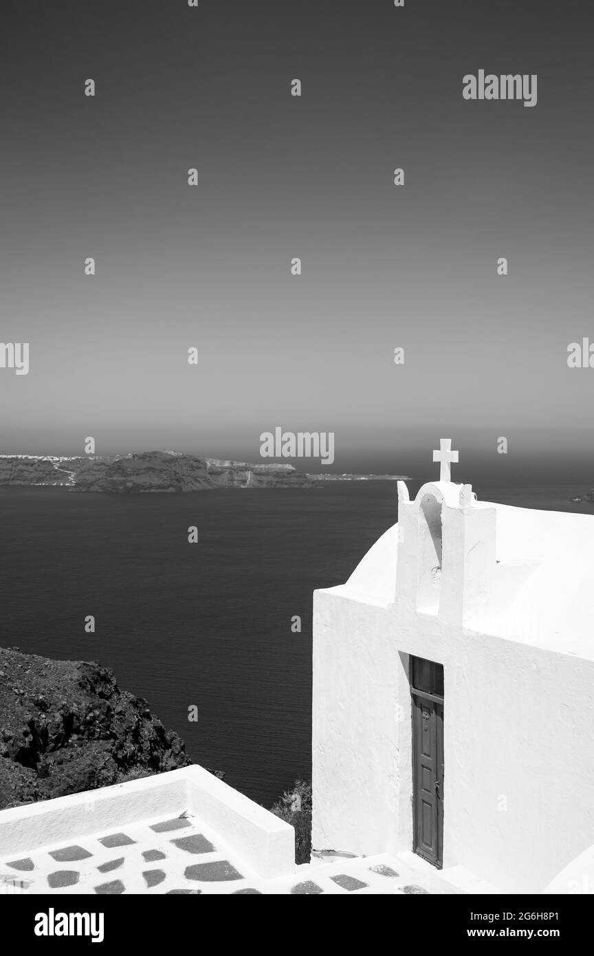 Santorini island. View of caldera at sunny day. Small minimalistic Greek Orthodox Church. White cross. Black and white. Stock Photo