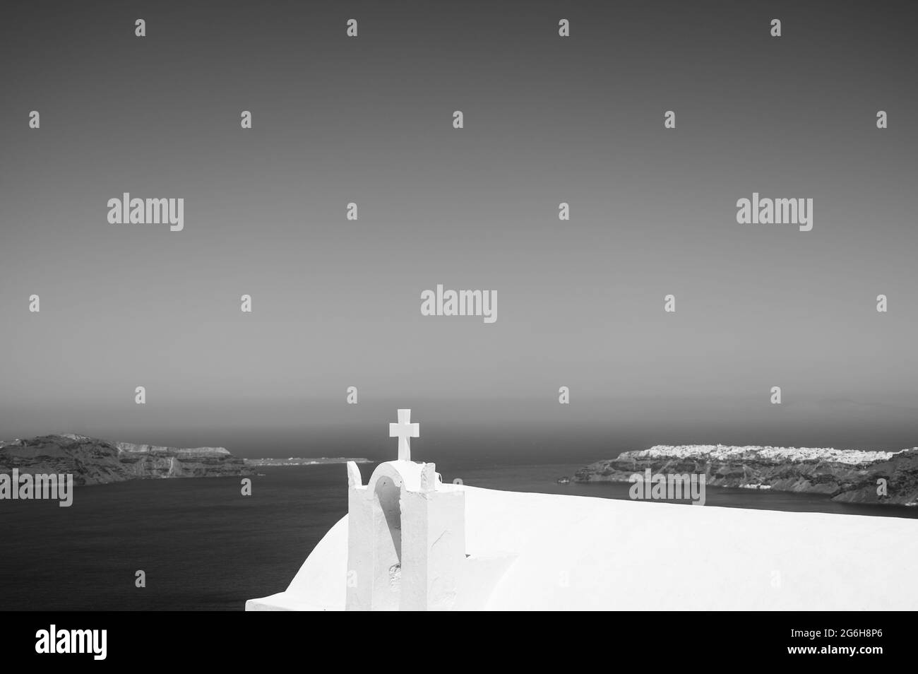 Santorini island. View of caldera at sunny day. Small minimalistic Greek Orthodox Church. Close-up of white cross. Black and white. Stock Photo