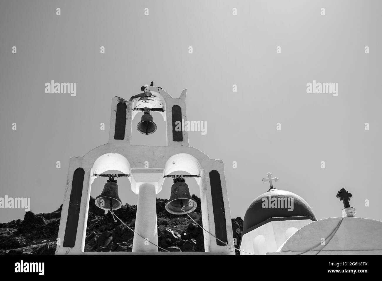 Bell tower of the traditional Greek Orthodox church on the island of Santorini. Sky and rock on background. Bottom view. Black and white. Stock Photo