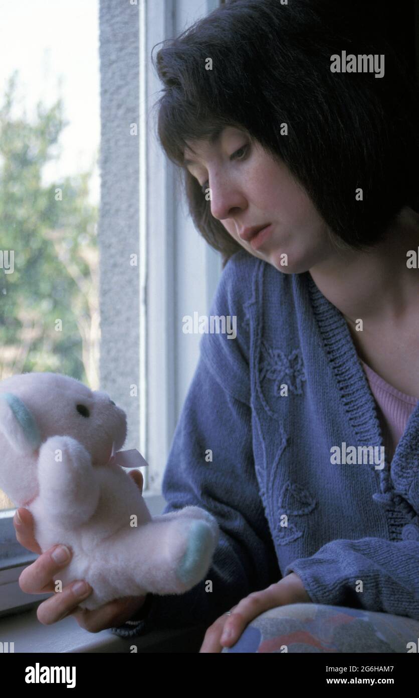 unhappy woman sitting by window holding teddy bear Stock Photo