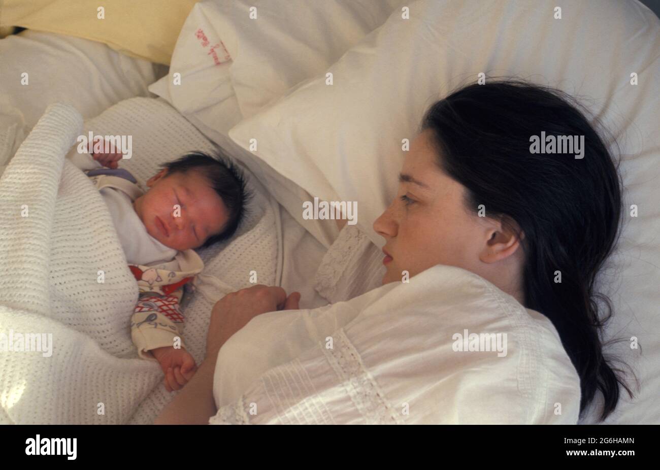 unhappy teenage mother lying in hospital bed with her newborn baby Stock Photo