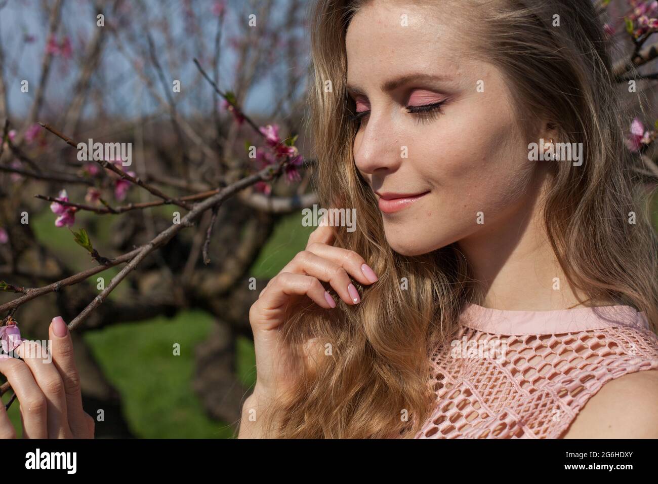 Beautiful blonde woman in pink dress in blossoming spring green garden Stock Photo